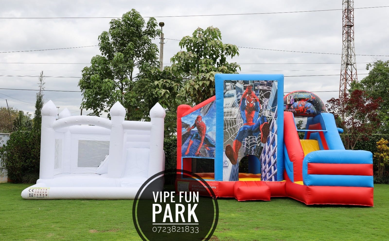 A white bouncing castle beside a red and blue superhero-themed inflatable on the lawn