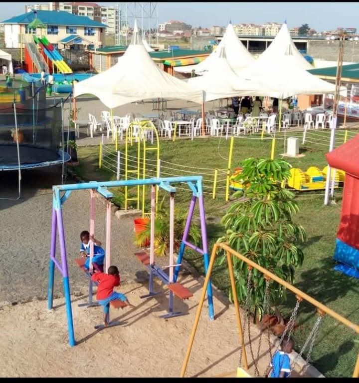 Children on colourful swings with tents and play structures across the park behind them