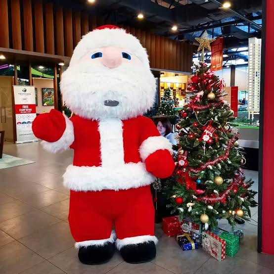 A festive Santa mascot costume standing beside a decorated Christmas tree
