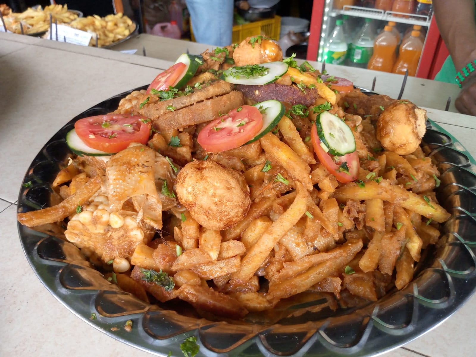 A large metal platter of chips, fried snacks, maize, tomato and cucumber served at Vipe Fun Park