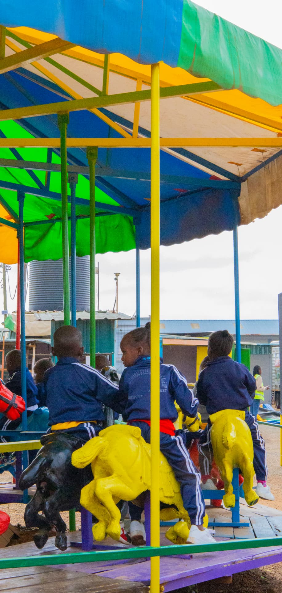 Children seen from behind riding yellow carousel horses beneath a colourful canopy