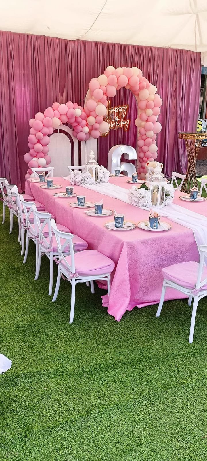 A pink birthday setup with a balloon arch, decorated table and white chairs at Vipe Fun Park